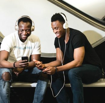 Two male students smiling and listening to music on headphones.
                  