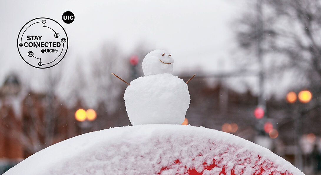 A snowman perched on a red half circle with tree line and traffic lights in the background