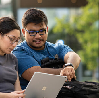 Male and female student working on a laptop outdoors.
                  