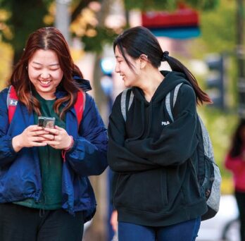 UIC student using her phone while friend looks on
                  