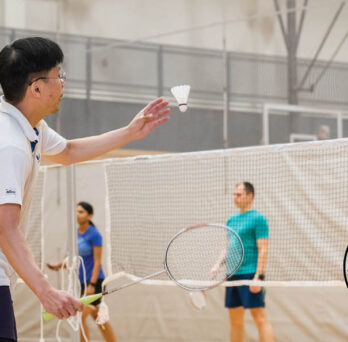 UIC student preparing a badminton serve with 3 students in the background
                  