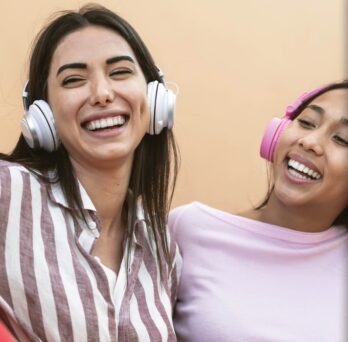 three female students enjoying music through headphones
                  