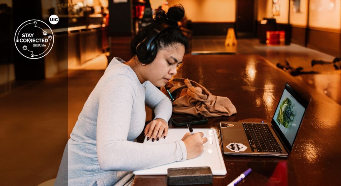 Student sitting at a desk writing on a notepad with headphones on.