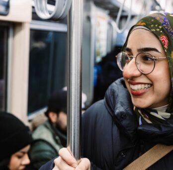 Female student holds bar while commuting on a bus.
                  