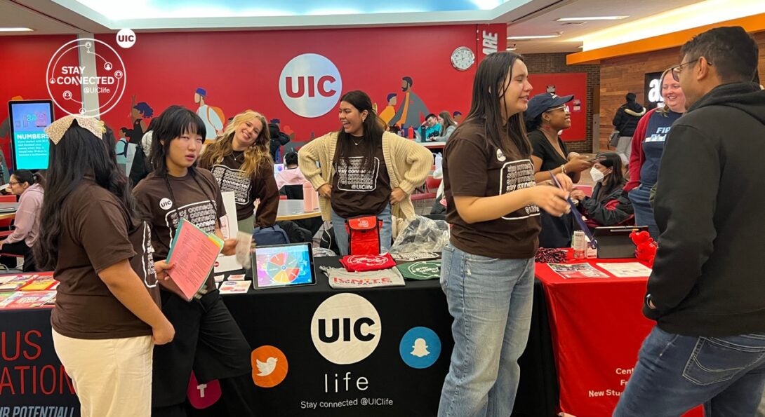 Student employees working at a table and talking to other students.