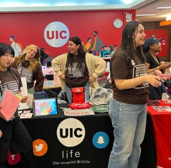 Student employees working at a table and talking to other students.
                  