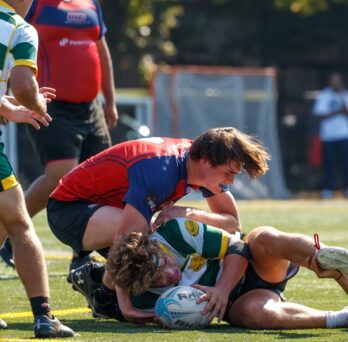 Men huddled around a rugby ball at a UIC home game.
                  